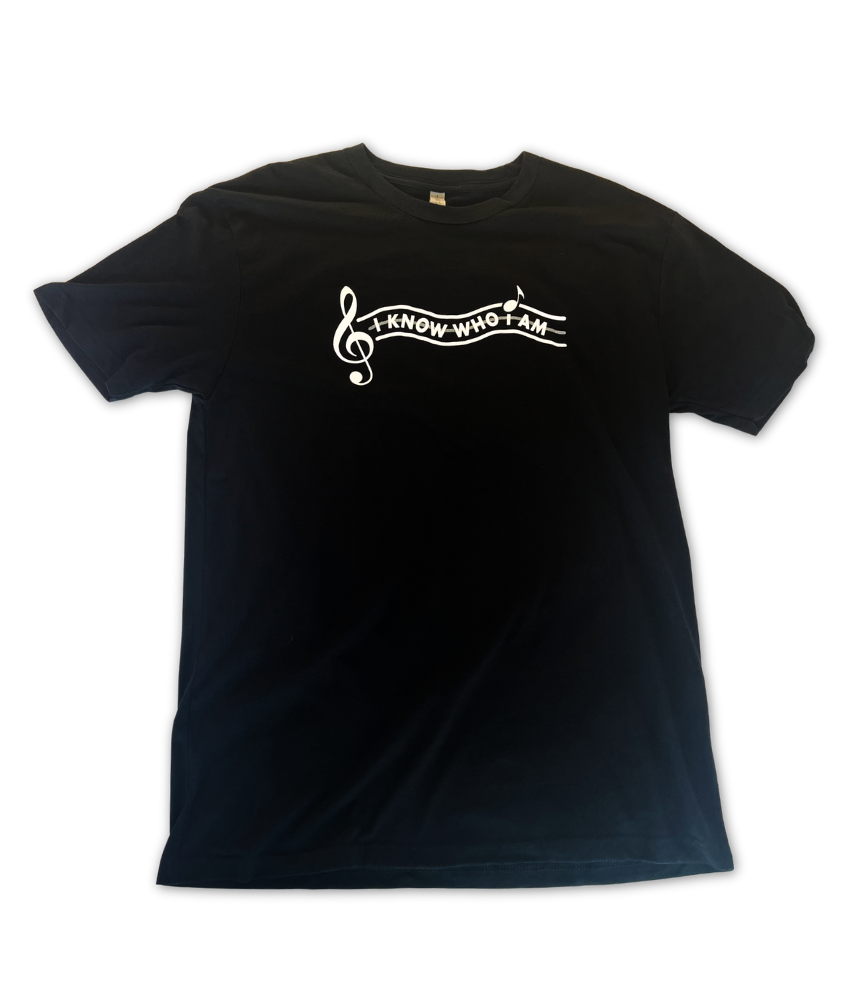 Image of a black t shirt with the text "I Know Who I Am" written on the front, next to a large treble clef