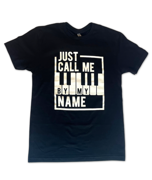 Image of a black t shirt with the words "Just call me by my name", stylized around a bordered piano keyboard