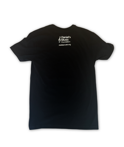 Rear image of a black t shirt with the Daniel's Music Logo on the back, featuring the foundation's name stacked, with a large treble clef to the left. Below, the URL danielsmusic.com is written.