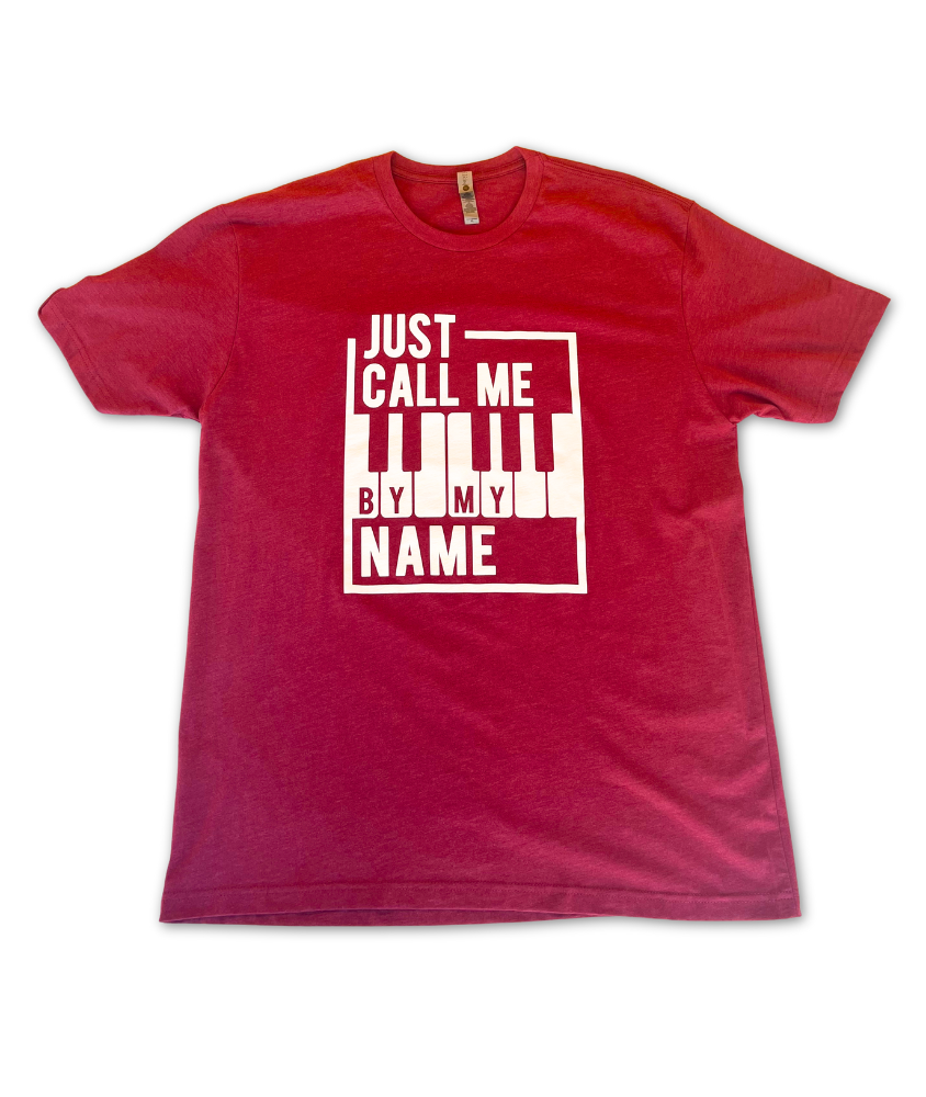 Image of a red t shirt with the words "Just call me by my name", stylized around a bordered piano keyboard