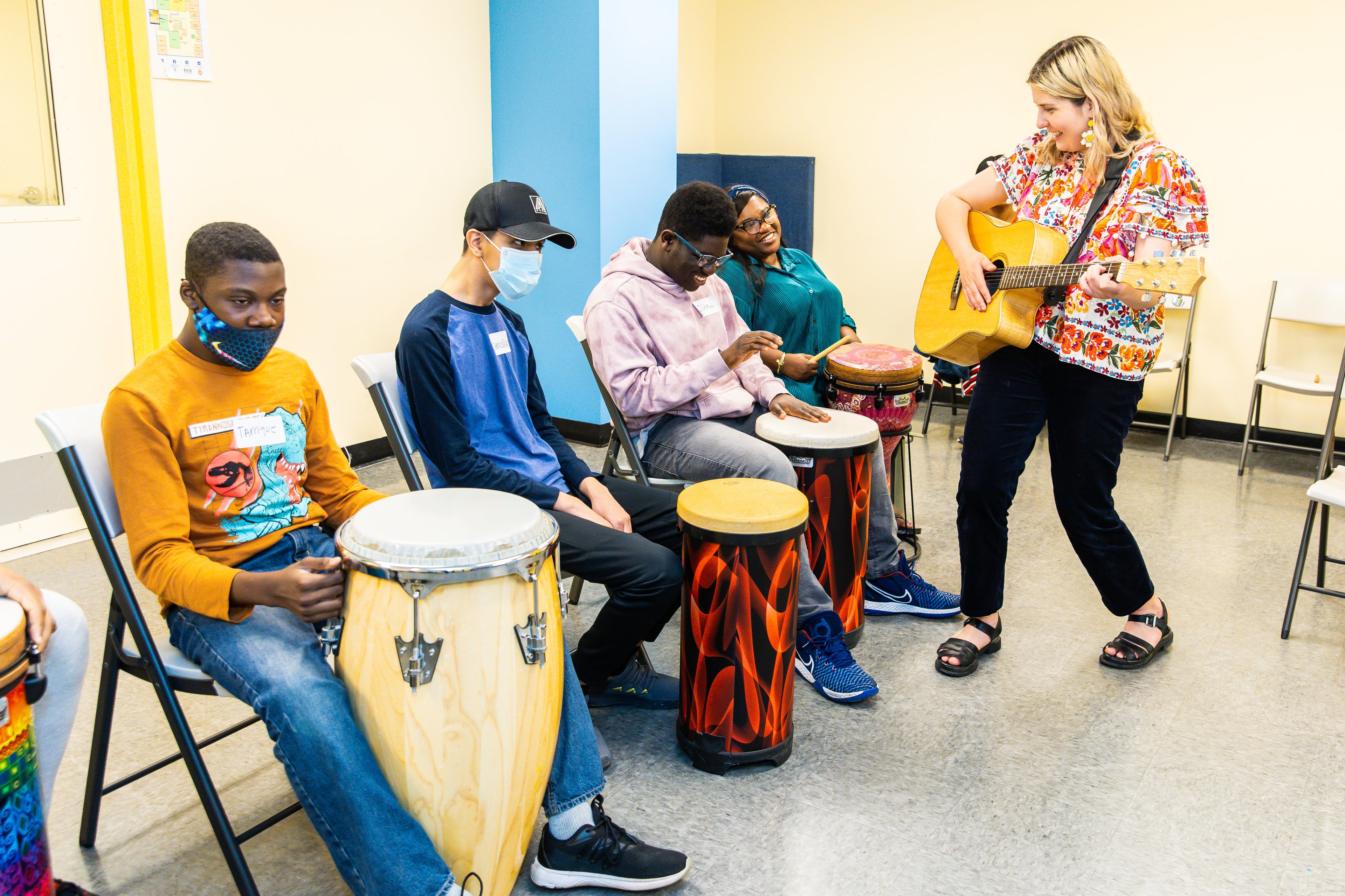 Image of a classroom at DMF. Students are playing conga drums while the teacher plays guitar next to them
